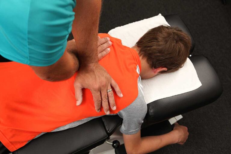 A person sitting in a car adjusting the seat and using a small pillow for lower back support.